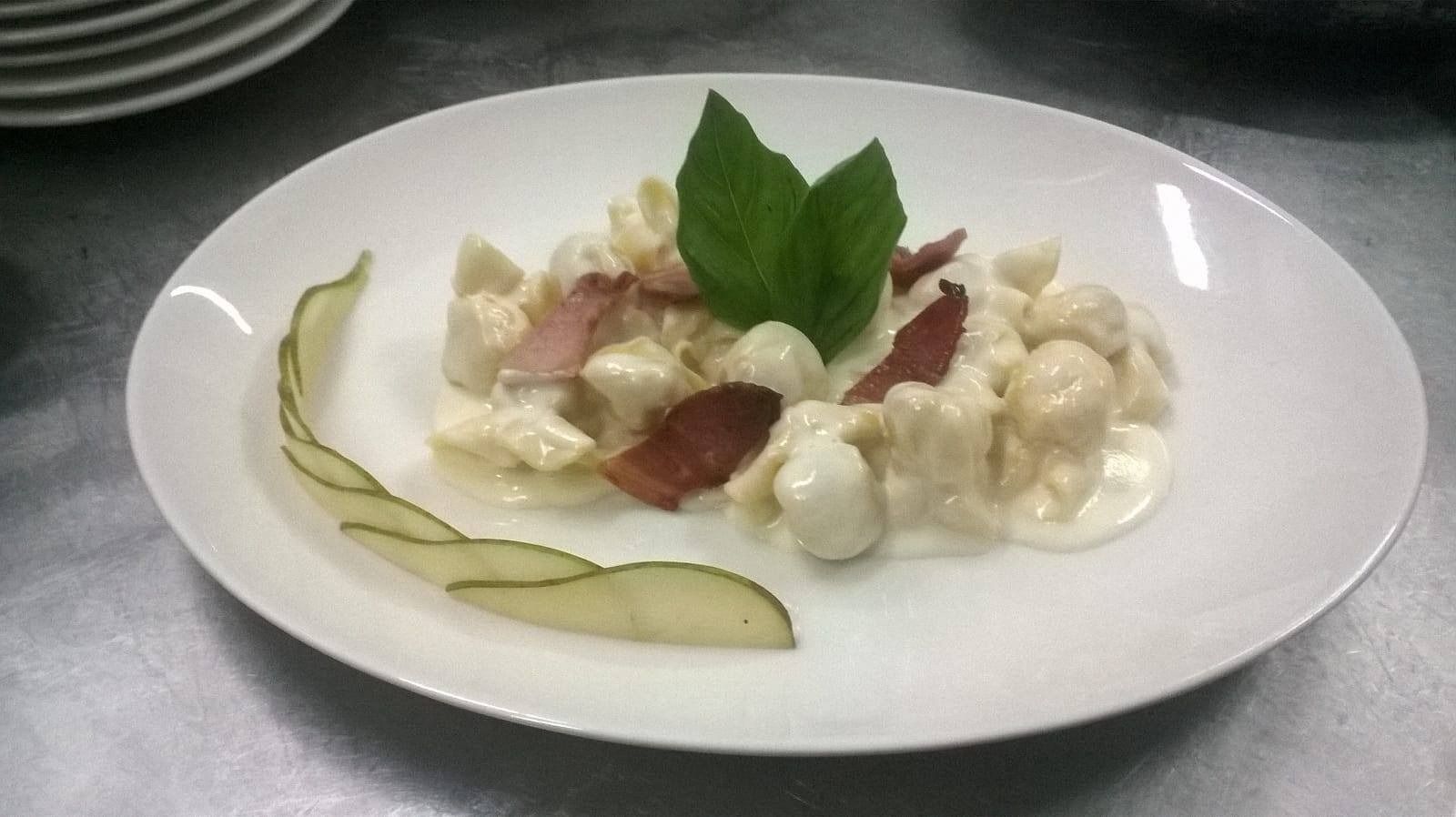 Un plato blanco cubierto de ñoquis y tocino sobre una mesa.