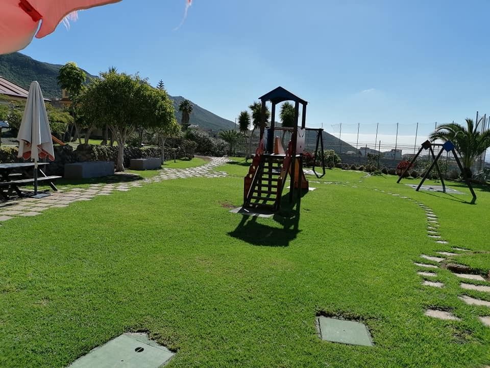 Un patio de juegos en un parque con una sombrilla roja en primer plano