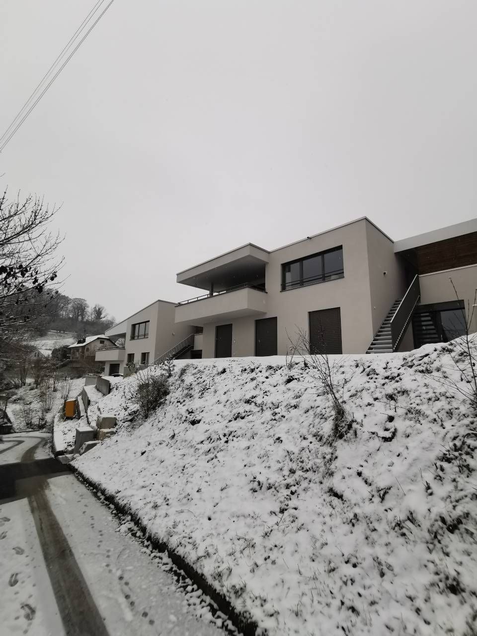 Schneebedeckter Hang mit modernen Häusern. Bewölkter Himmel. Eine Strasse führt zu den Häusern.