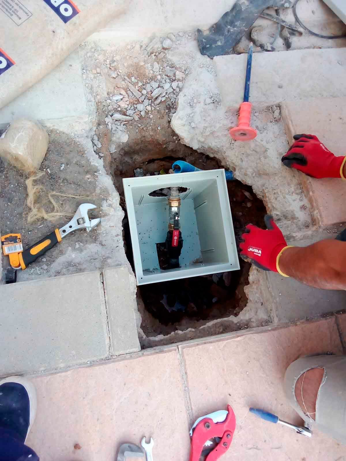 Una persona está arreglando una tubería en un agujero en el suelo.