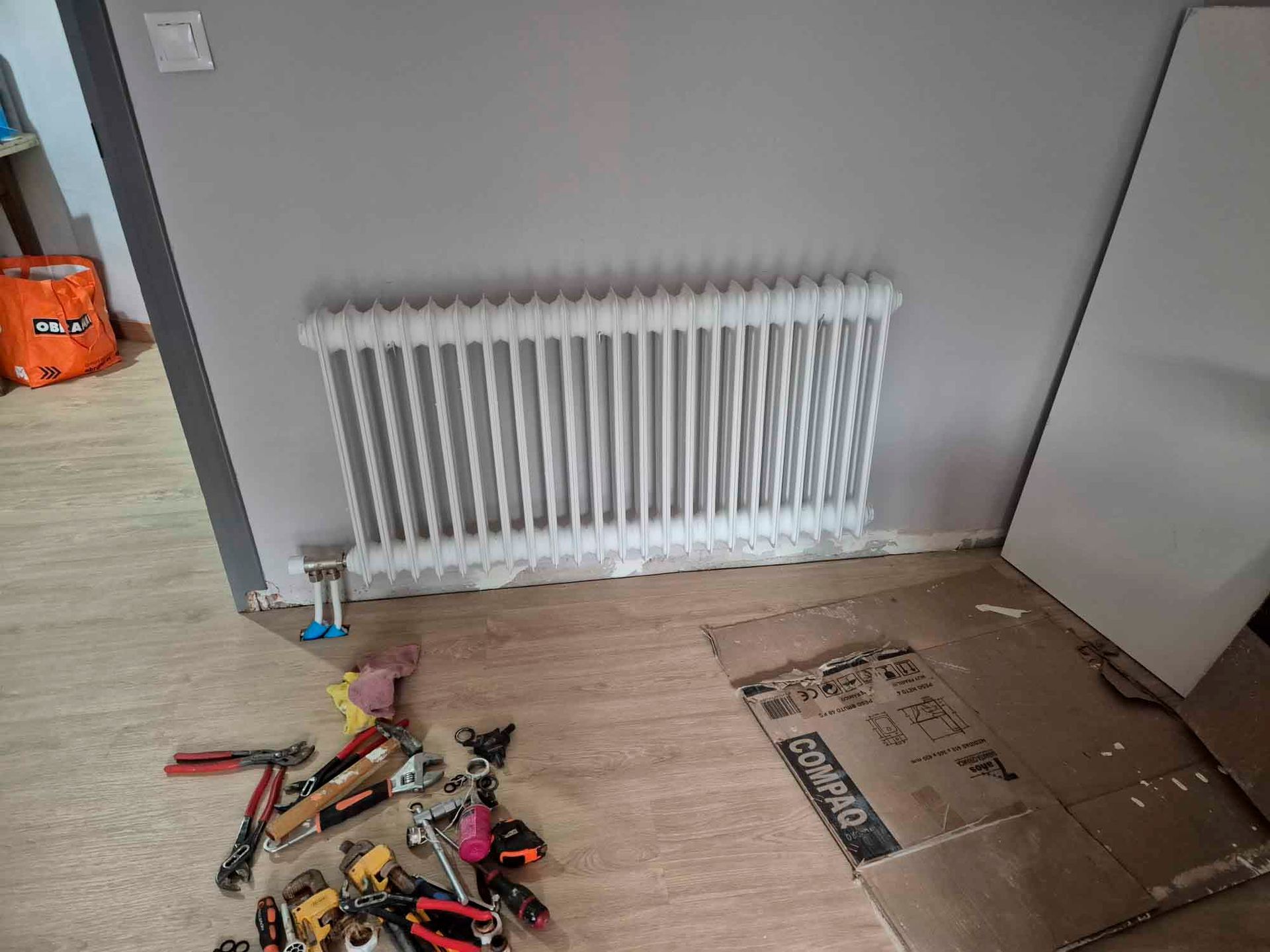Un radiador blanco está sobre un piso de madera al lado de una pila de herramientas.