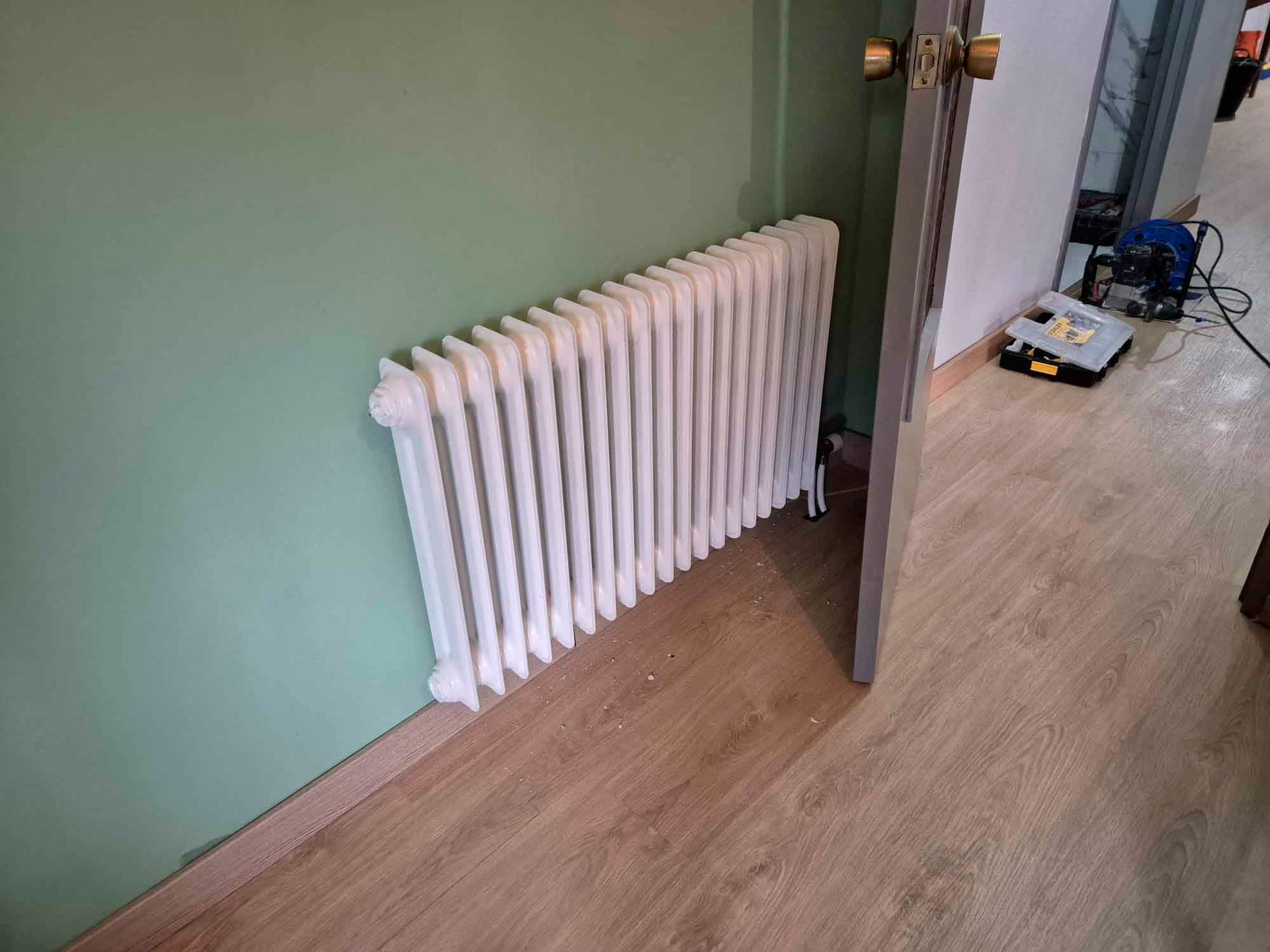 Un radiador blanco está sobre un piso de madera al lado de una puerta.