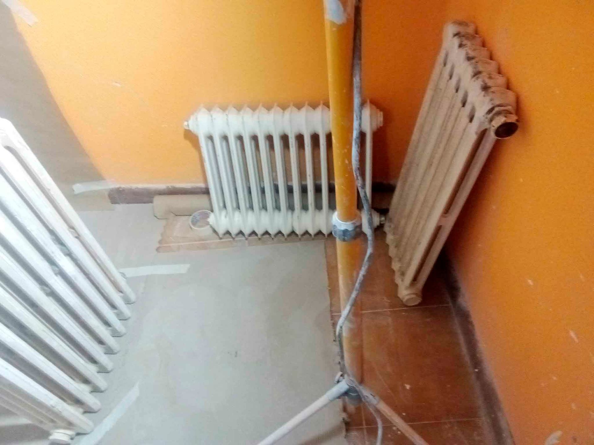 Una habitación con una pared naranja y un radiador en el suelo.
