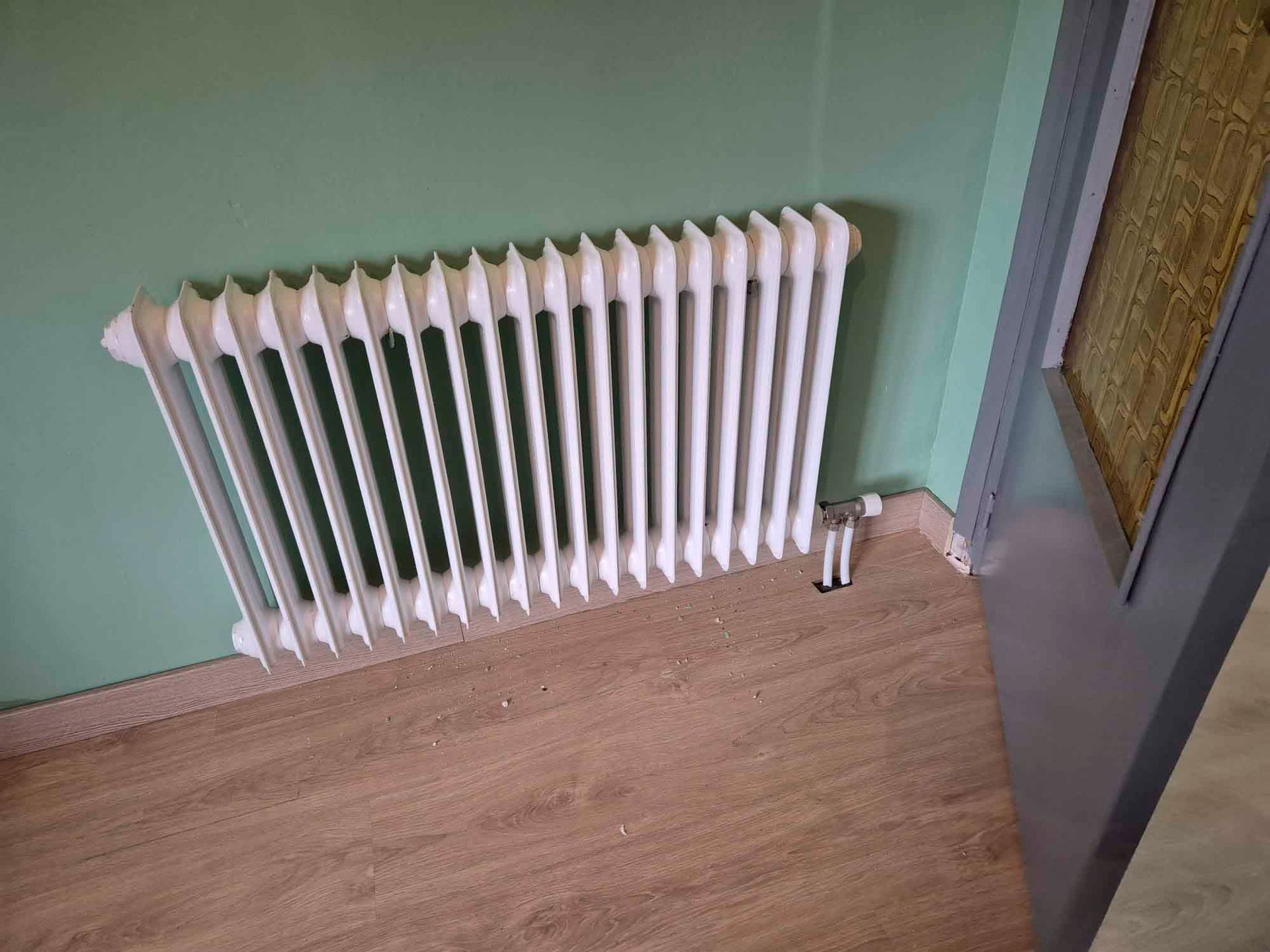 Un radiador blanco está sobre un piso de madera en una habitación al lado de una puerta.