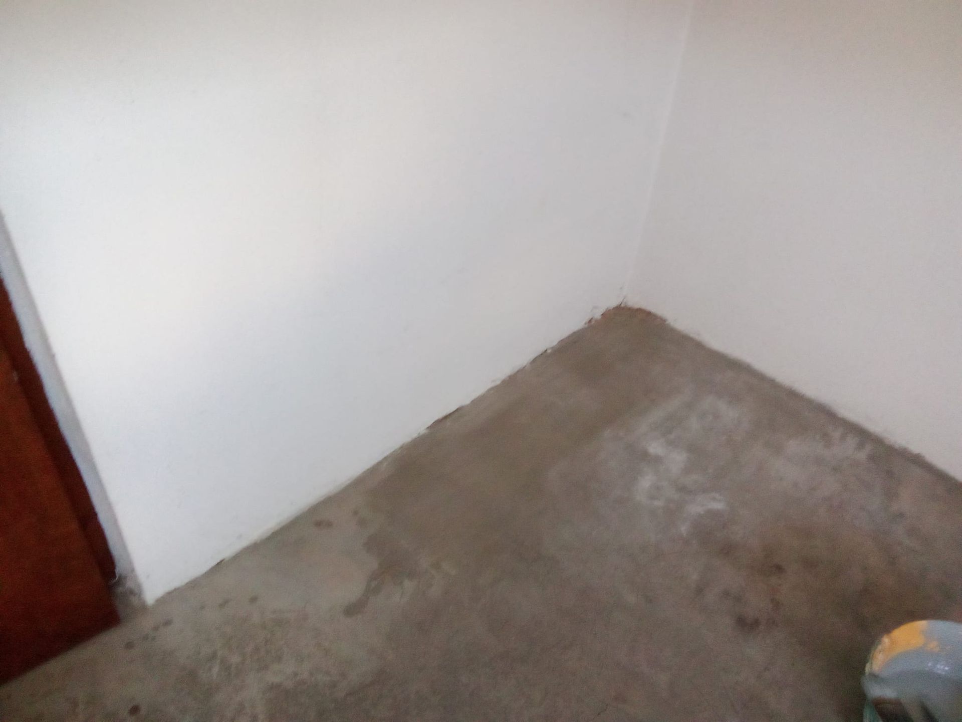 Un rincón de una habitación con suelo de cemento y una pared blanca.