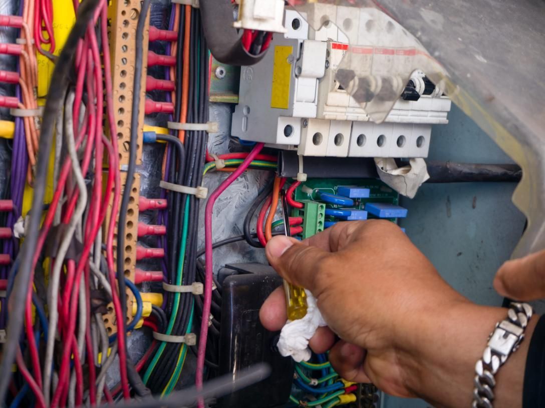 Ajuste manual del cableado dentro de un panel eléctrico abierto con cables multicolores y disyuntores.