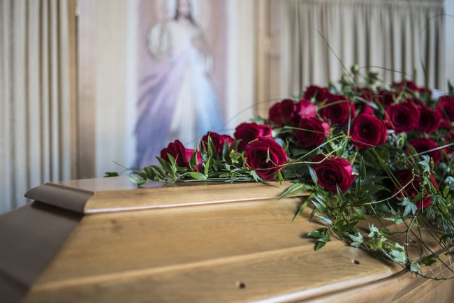 Cercueil fermé recouvert de roses rouges dans une église.