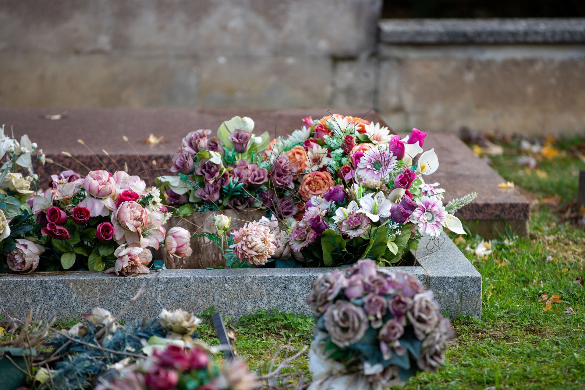 Tombe recouverte de fleurs et de bouquets colorés dans un cimetière.