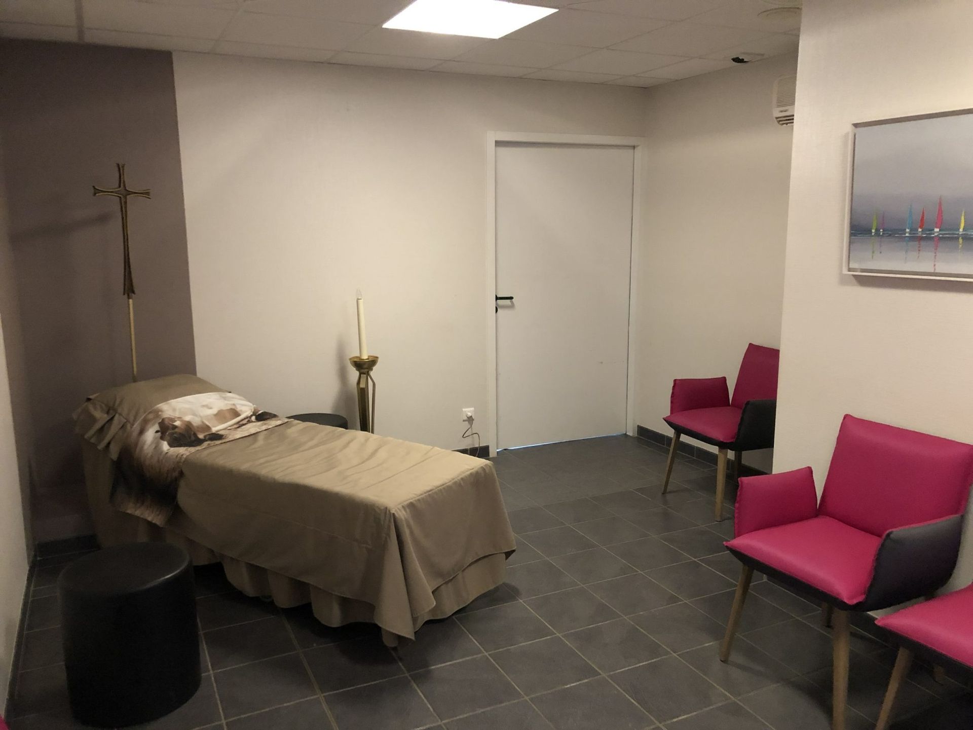 Chambre funéraire avec un lit, deux chaises roses et une porte fermée.