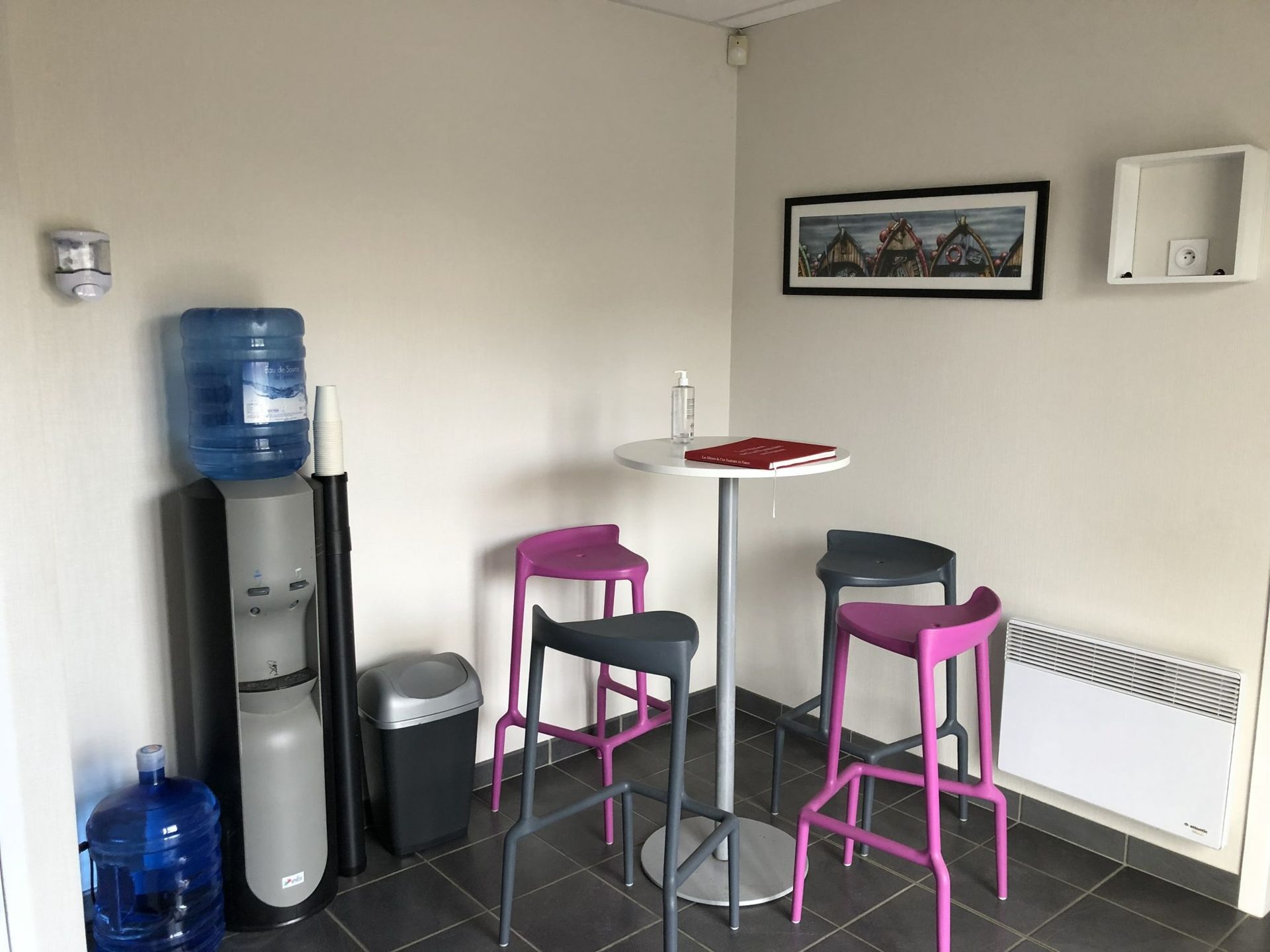 Petite salle de pause avec fontaine à eau, tabourets, table haute et décorations murales.