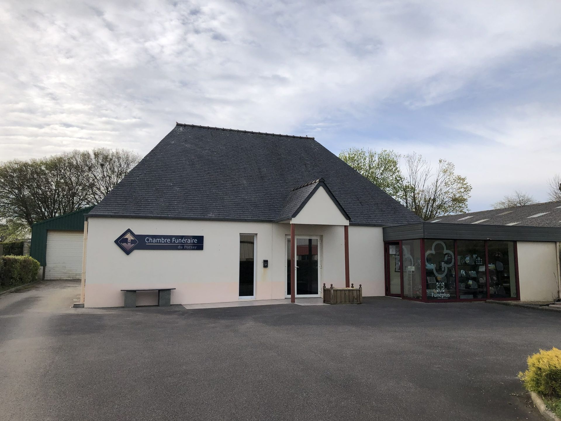 Petit bâtiment blanc au toit et à l'enseigne sombres, donnant sur un stationnement goudronné sous un ciel nuageux.