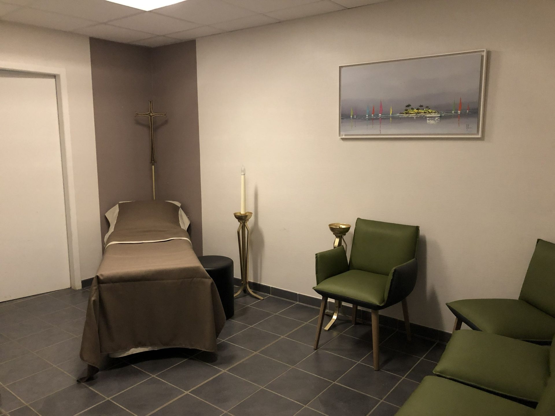 Chambre funéraire avec un lit, des chaises vertes et un paysage encadré au mur.