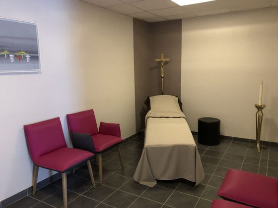 Chambre funéraire avec un lit, un crucifix, des bougies et des chaises magenta le long du mur.