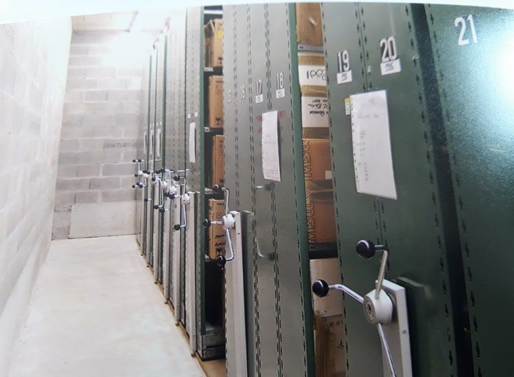 Rangée d'étagères mobiles vertes remplies de dossiers dans une pièce aux murs en béton.