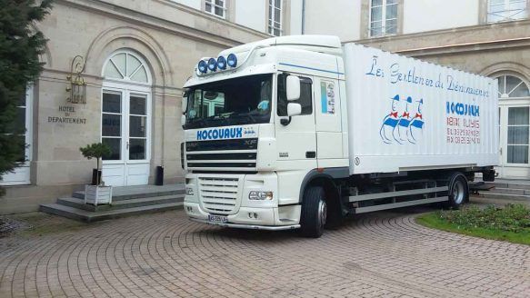 Un semi-remorque blanc est garé devant un bâtiment à colonnes et portes.