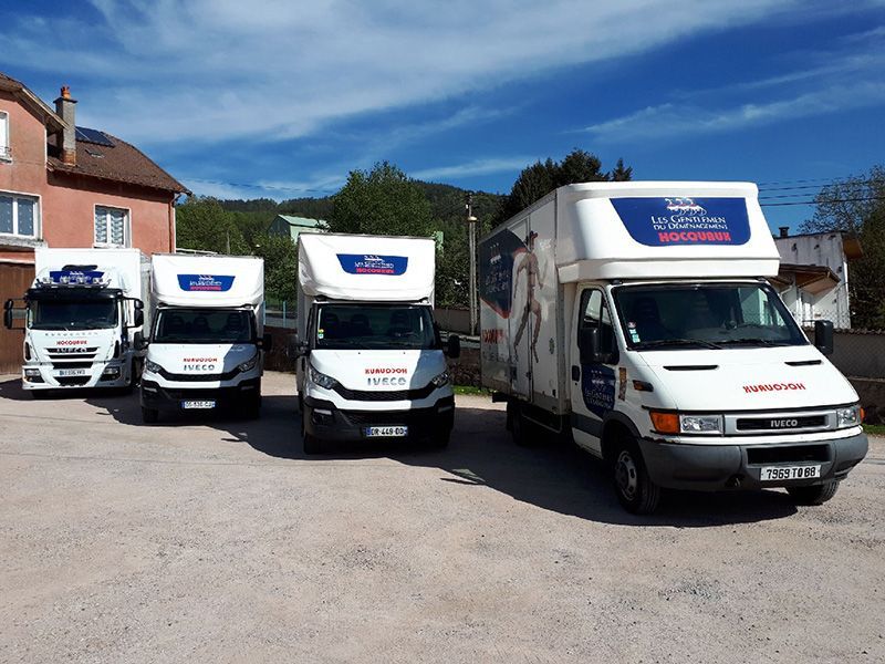 Quatre camions de livraison blancs étaient garés devant un bâtiment par une journée ensoleillée.