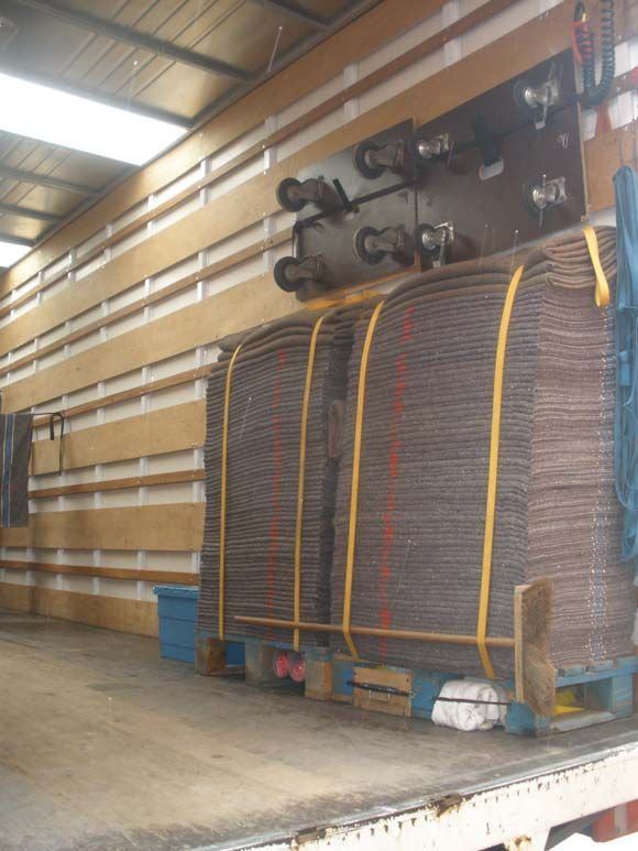 À l'intérieur d'un camion, des piles de grilles métalliques brunes, maintenues par des sangles jaunes, sur une palette en bois.