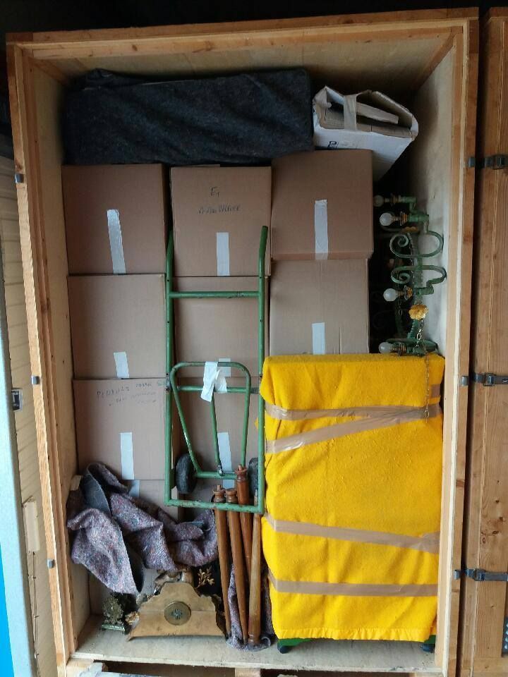 Un box de stockage rempli de cartons, de meubles emballés en jaune, d'un diable et d'objets divers.
