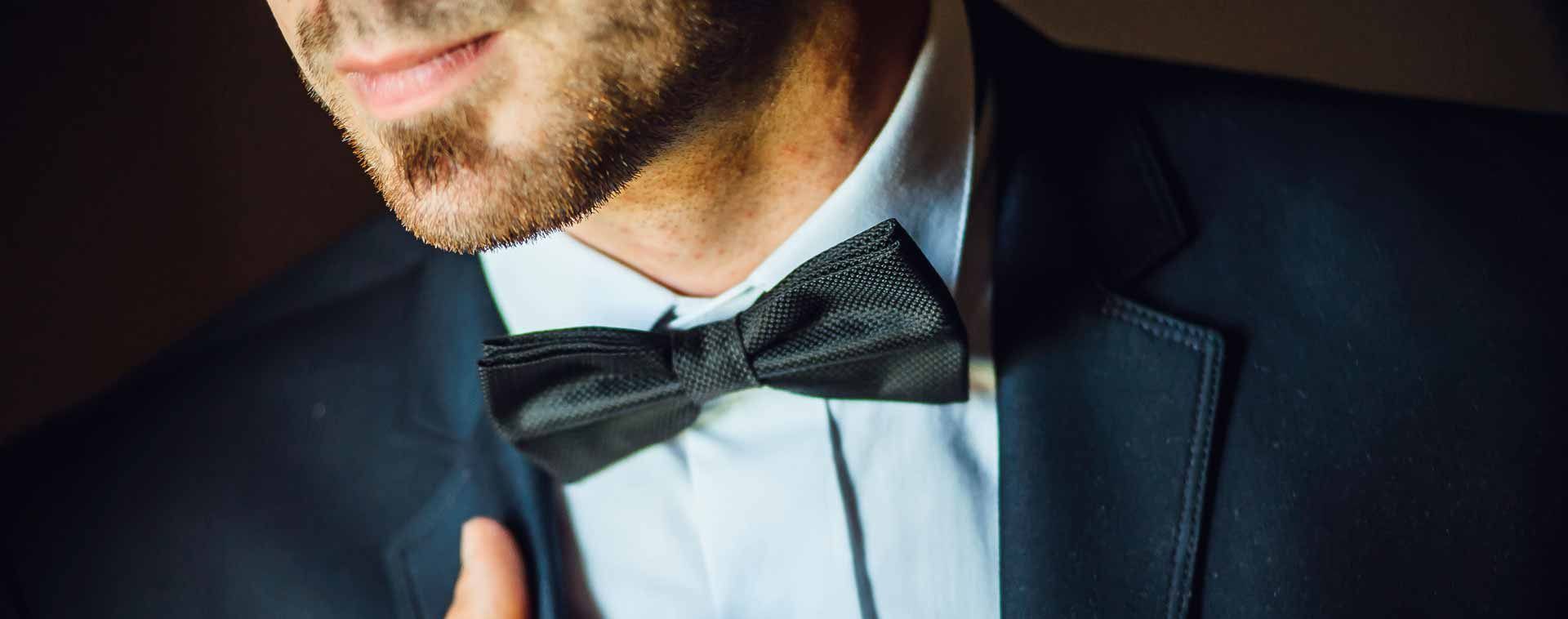 Homme en costume bleu marine et nœud papillon noir, avec une chemise à col bleu clair.