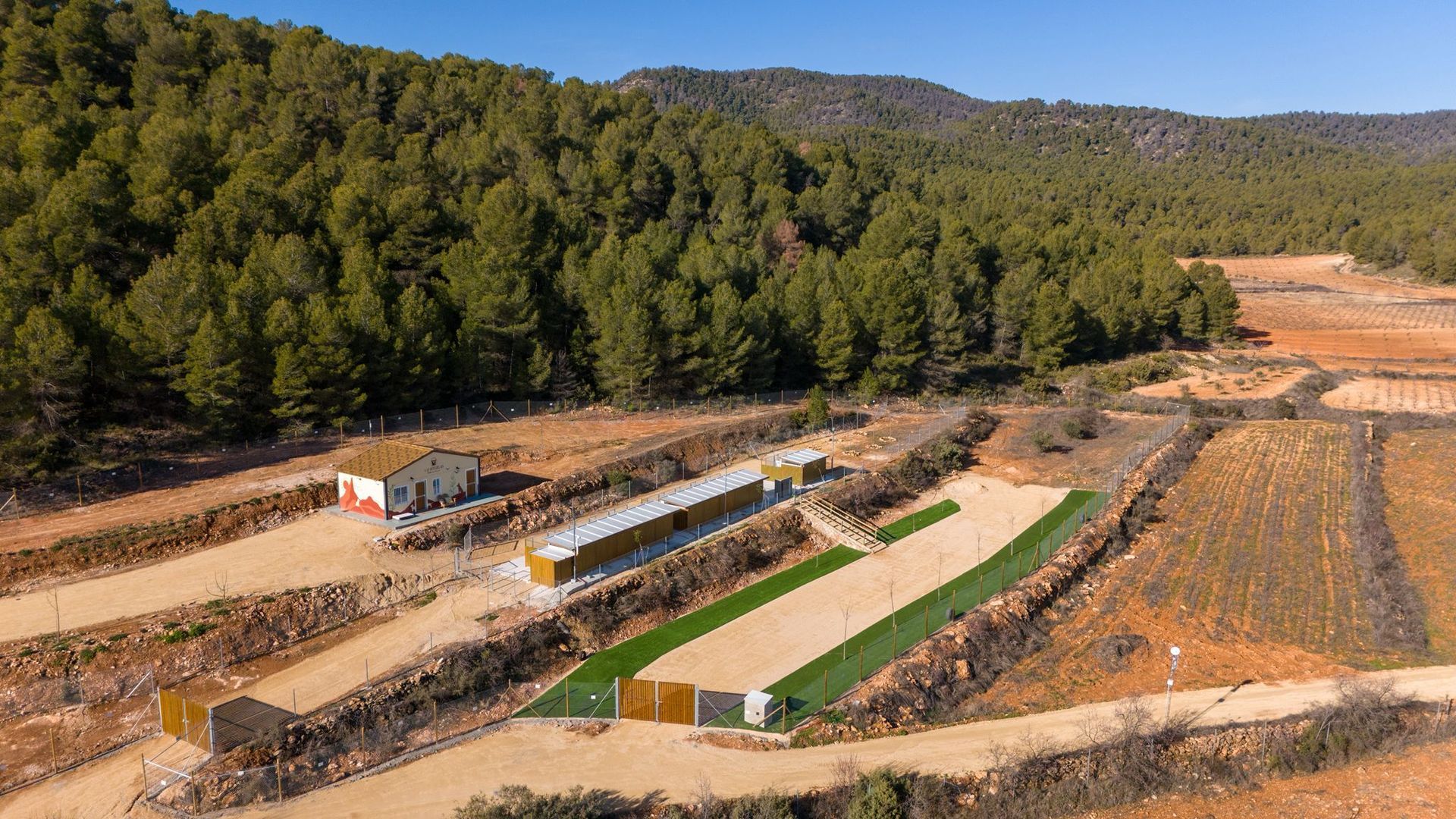 Vista aérea de una gran obra de construcción al aire libre con largas zanjas bordeadas de vegetación y árboles circundantes.