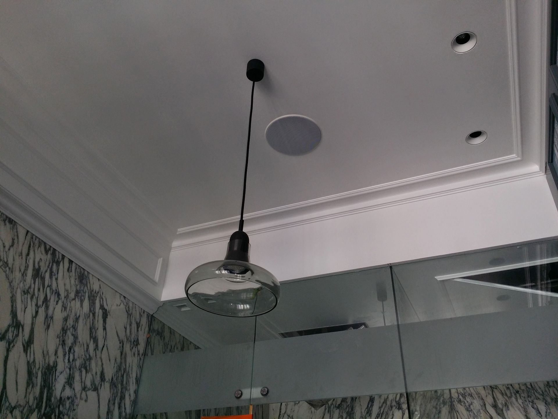 Plafond de salle de bain avec un luminaire suspendu et des spots encastrés au-dessus d'une paroi de douche en verre.
