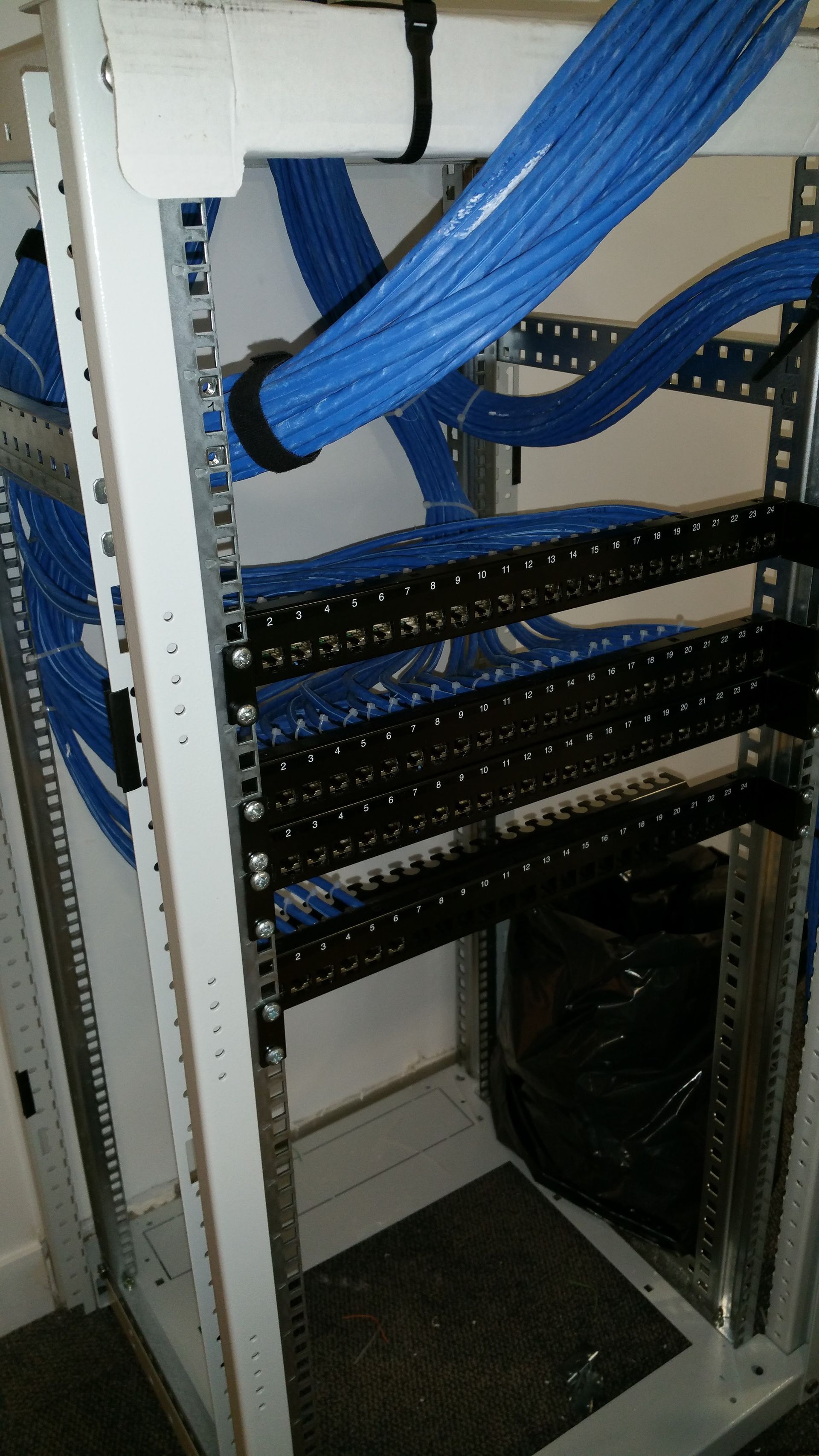 Panneau de brassage de câbles réseau dans une baie de serveurs, avec des câbles Ethernet bleus connectés et regroupés.
