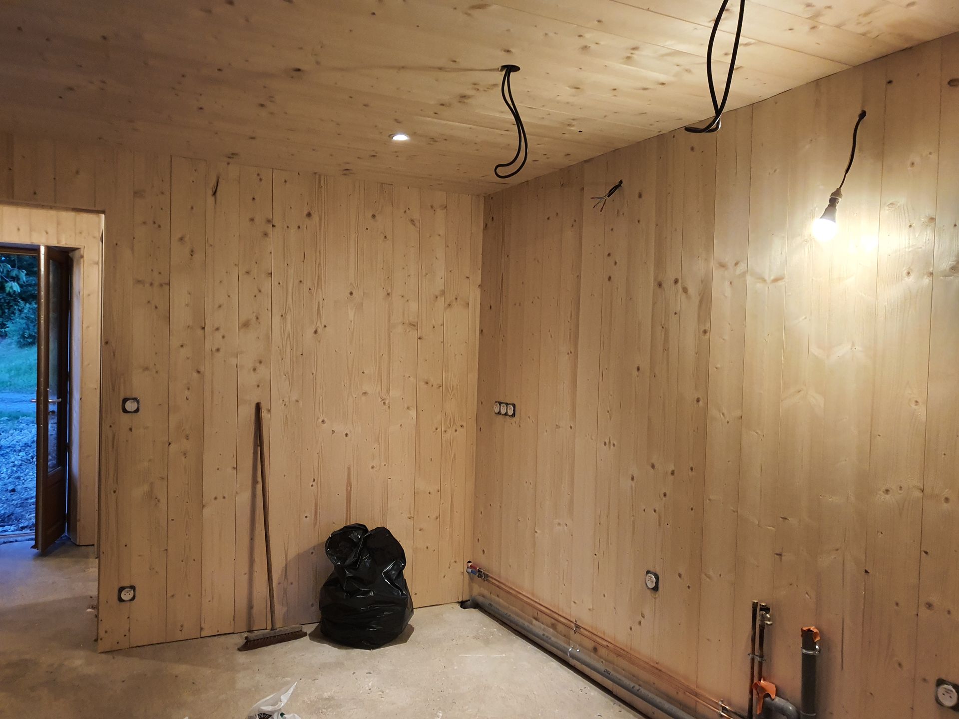 Intérieur en travaux avec lambris en bois, câbles électriques au plafond et arrivée d’eau visible.