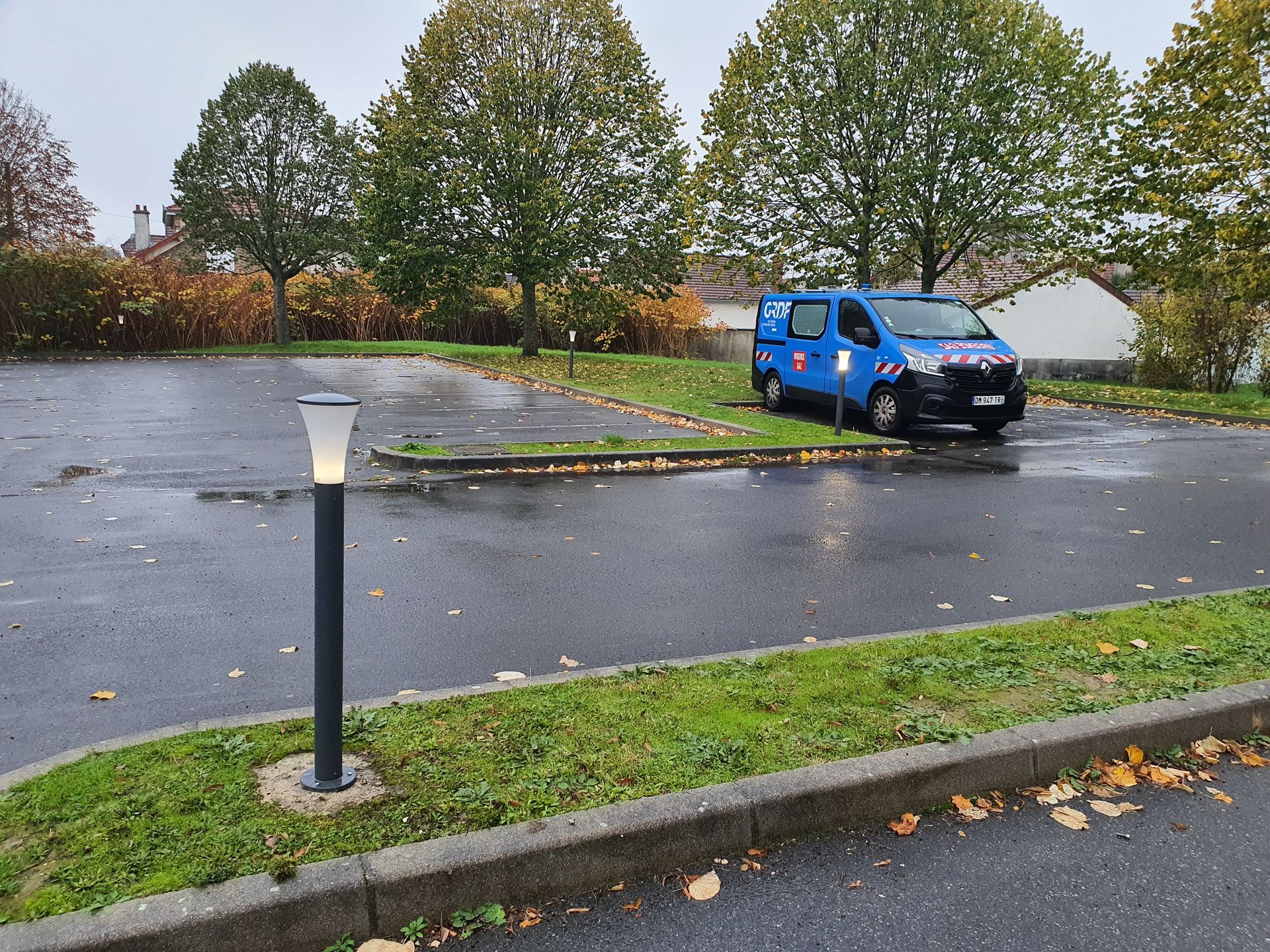 Une camionnette GRDF bleue garée sur un parking mouillé, dans une zone résidentielle.