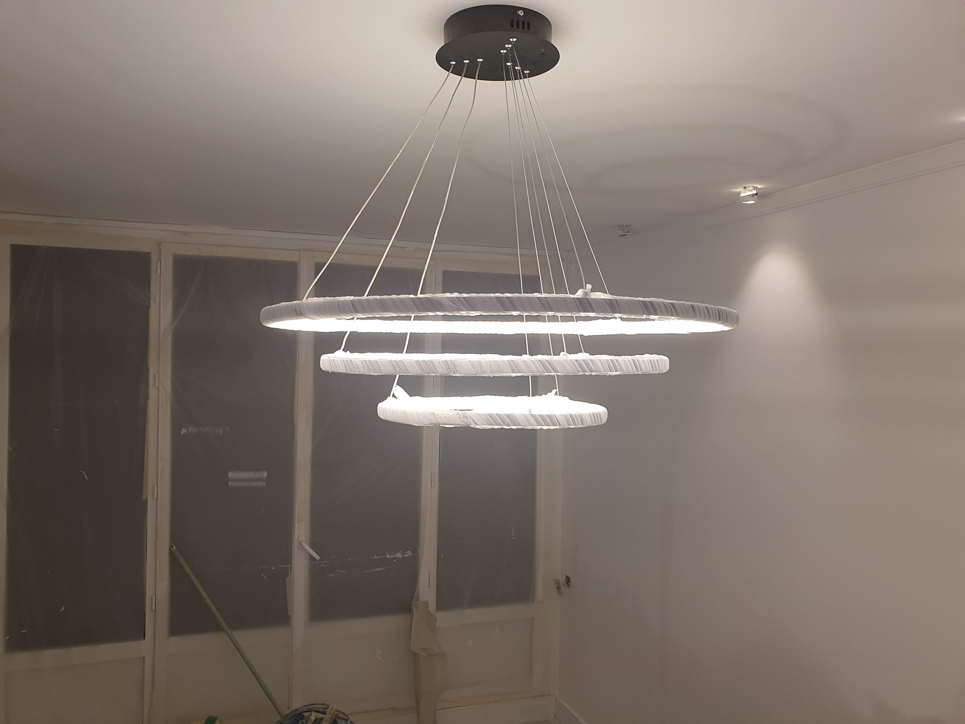 Un lustre suspendu moderne illumine une pièce en rénovation avec de grandes fenêtres.