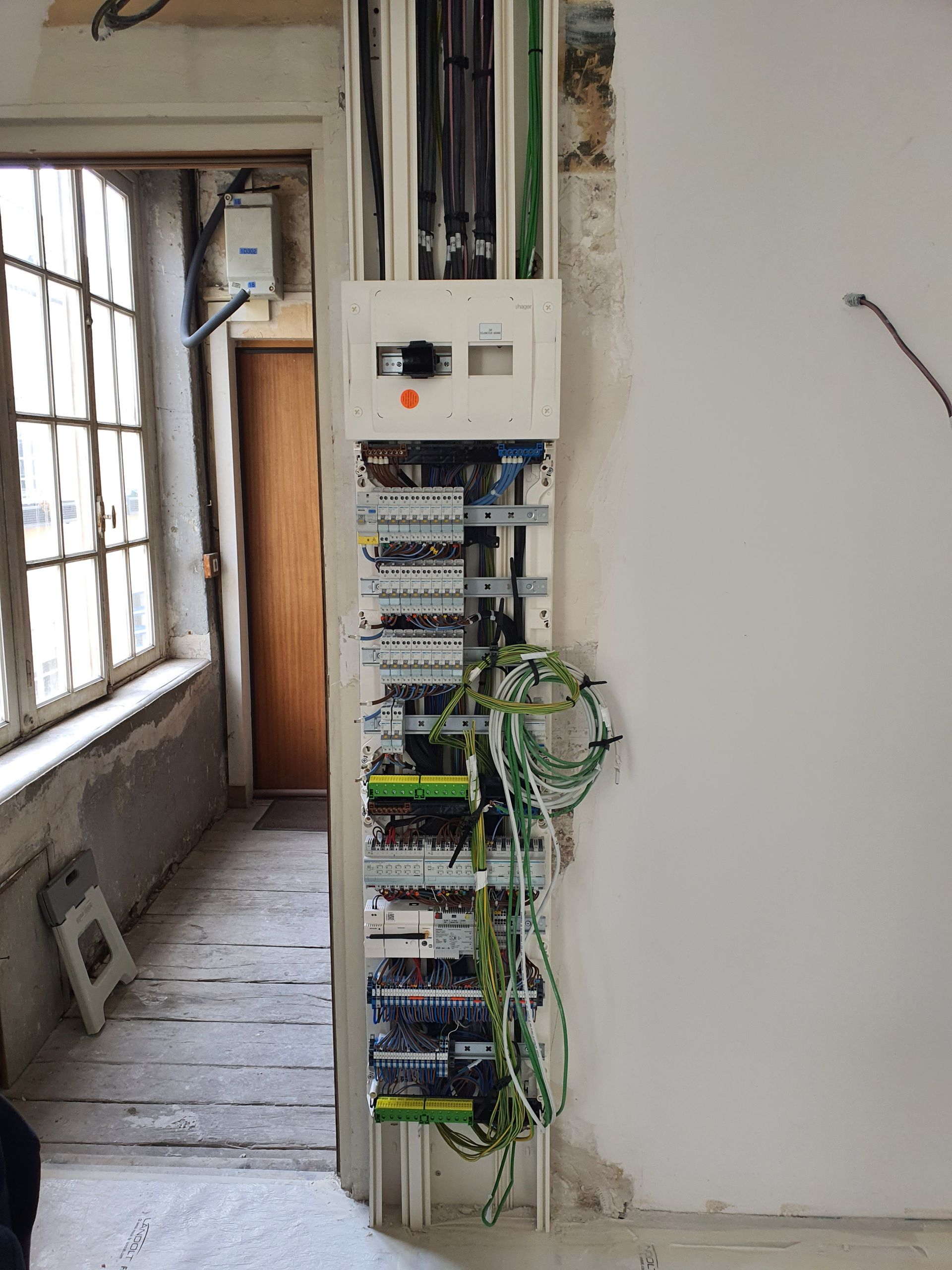 Installation électrique en cours avec tableau encastré, disjoncteurs et câbles visibles dans un intérieur en rénovation.