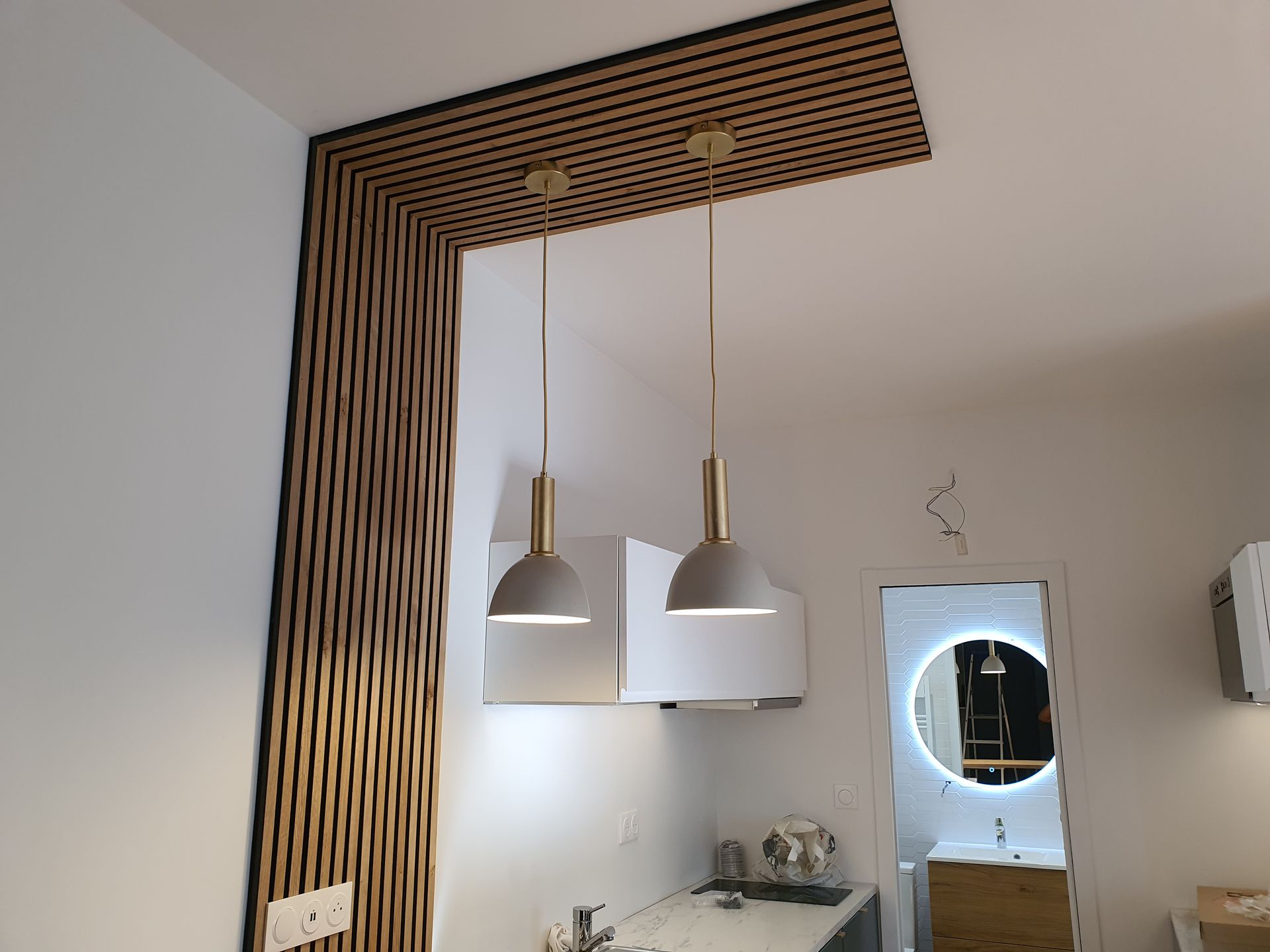 Aménagement intérieur avec claustra en bois, plan de travail et suspensions design au-dessus d’une cuisine.