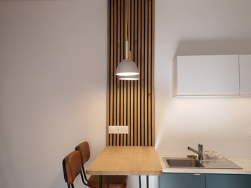 Coin cuisine moderne avec table en bois, chaises, suspensions lumineuses blancs et lambris mural.