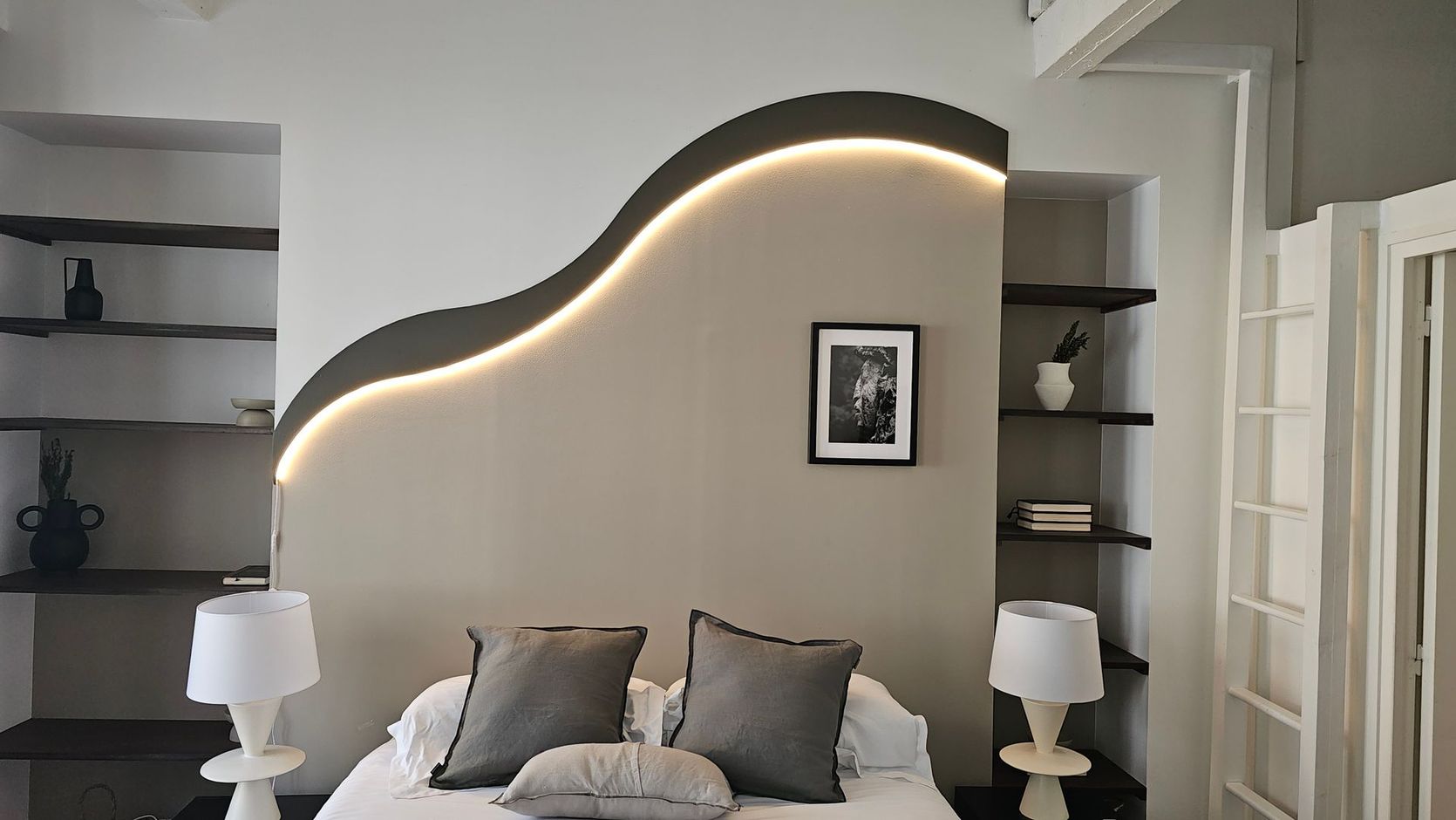 Chambre moderne avec une tête de lit ondulée lumineuse, des niches murales et des murs blancs.