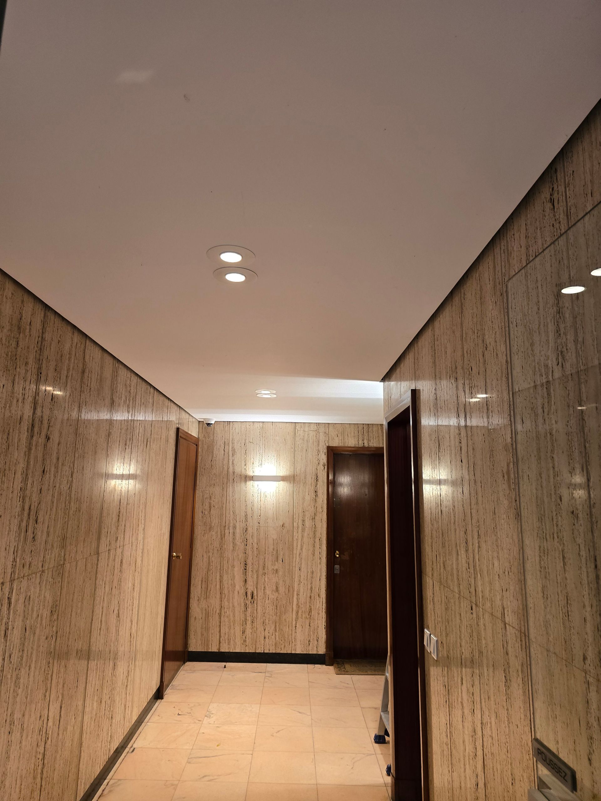 Couloir avec spots encastrés au plafond et des portes en bois.
