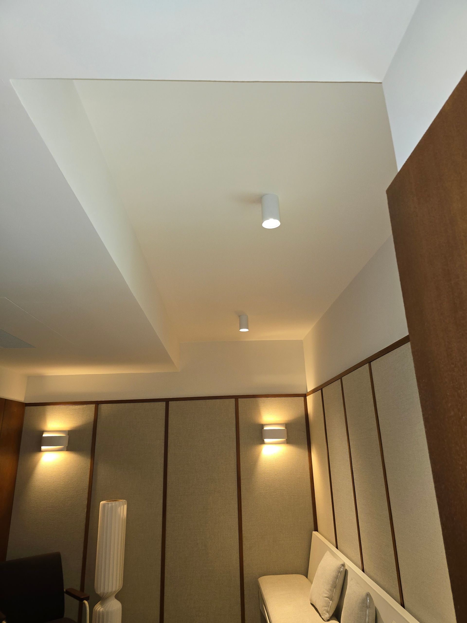 Chambre d'hôtel moderne avec murs beiges, éclairage au plafond, éléments en bois et canapé le long du mur de droite.