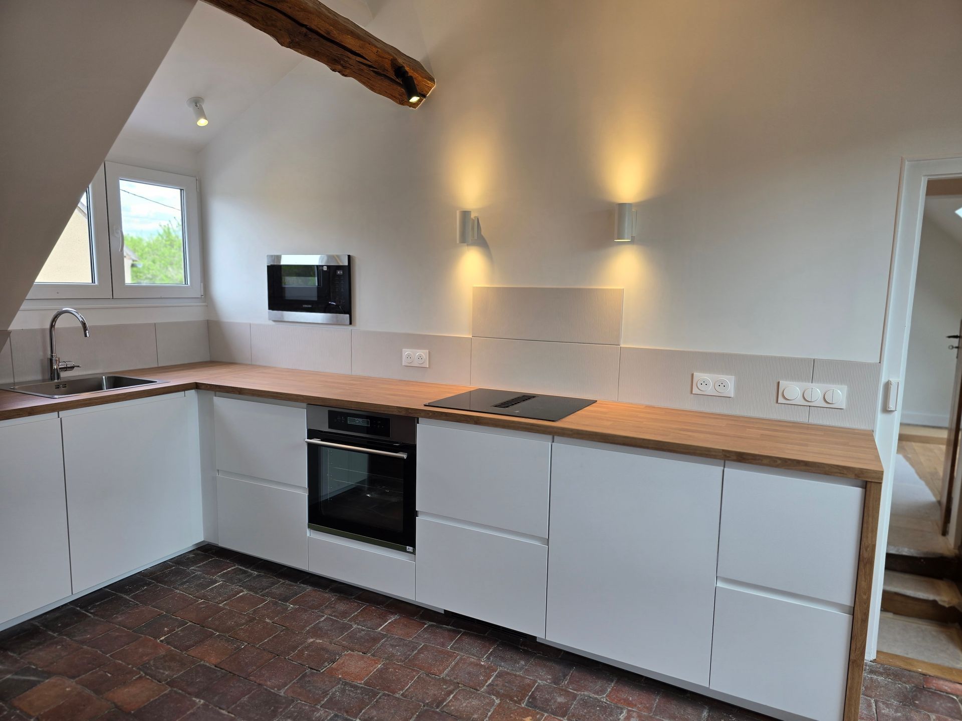 Cuisine neuve avec placards blancs, plan de travail en bois, four noir et sol en pierre.