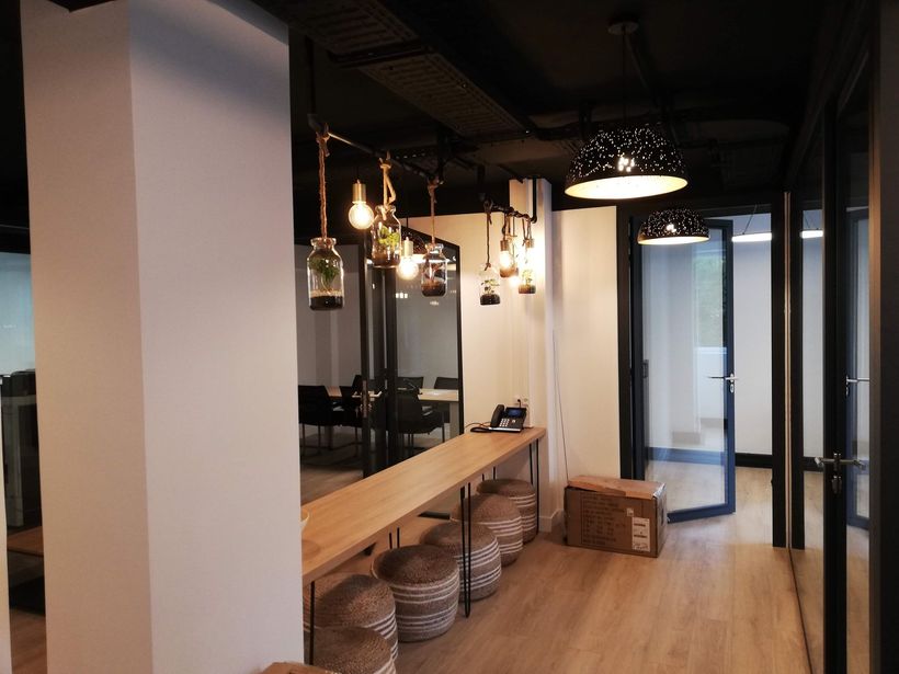 Intérieur de café moderne avec comptoir en bois, luminaires suspendus, tabourets en osier et portes vitrées.