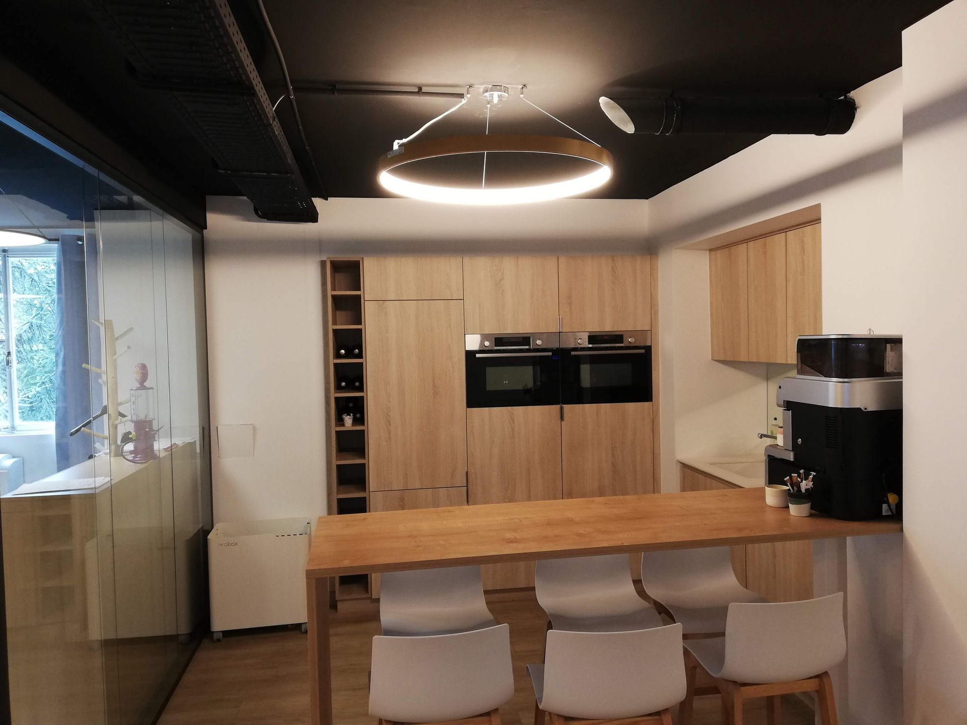 Cuisine contemporaine équipée avec meubles en bois, double four, îlot central et suspension lumineuse circulaire.