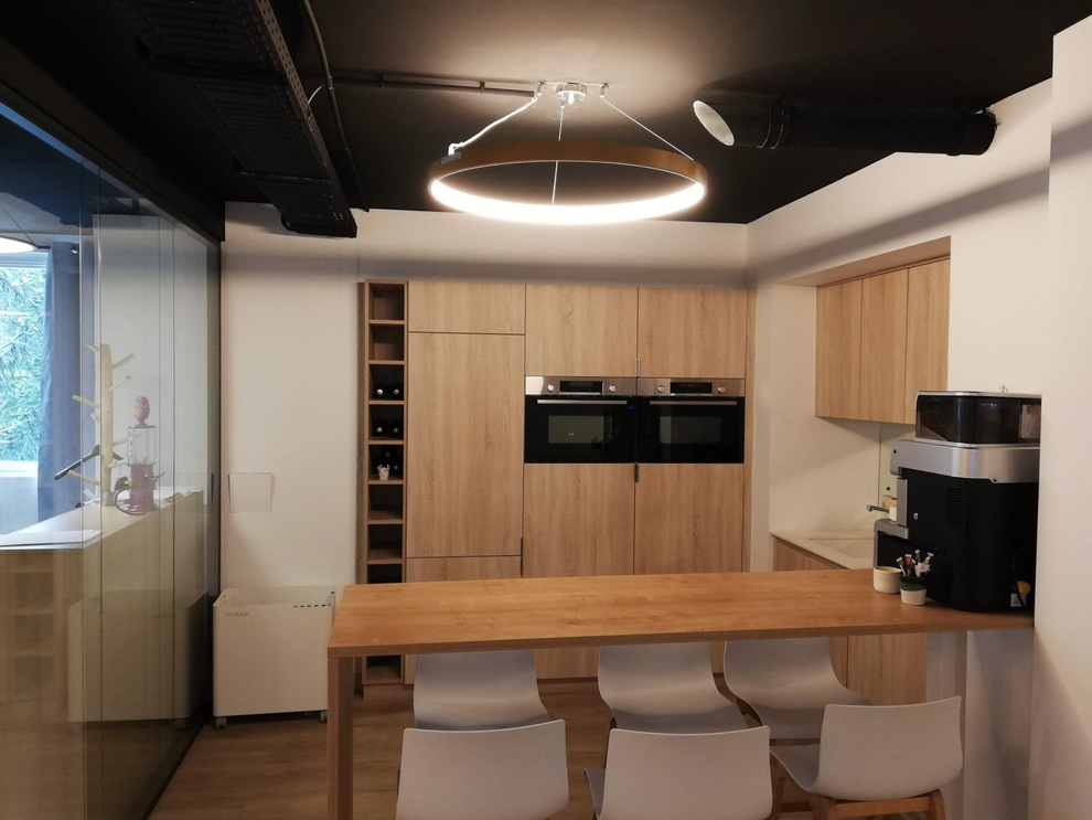 Cuisine contemporaine équipée avec meubles en bois, double four, îlot central et suspension lumineuse circulaire.