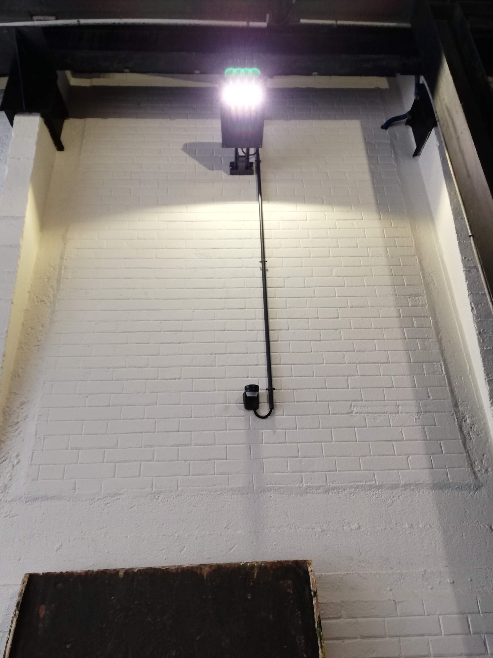 Caméra de sécurité fixée au plafond avec un éclairage puissant au-dessus d'un mur au carrelage métro blanc.