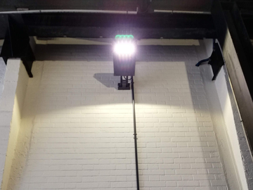 Caméra de sécurité fixée au plafond avec un éclairage puissant au-dessus d'un mur au carrelage métro blanc.