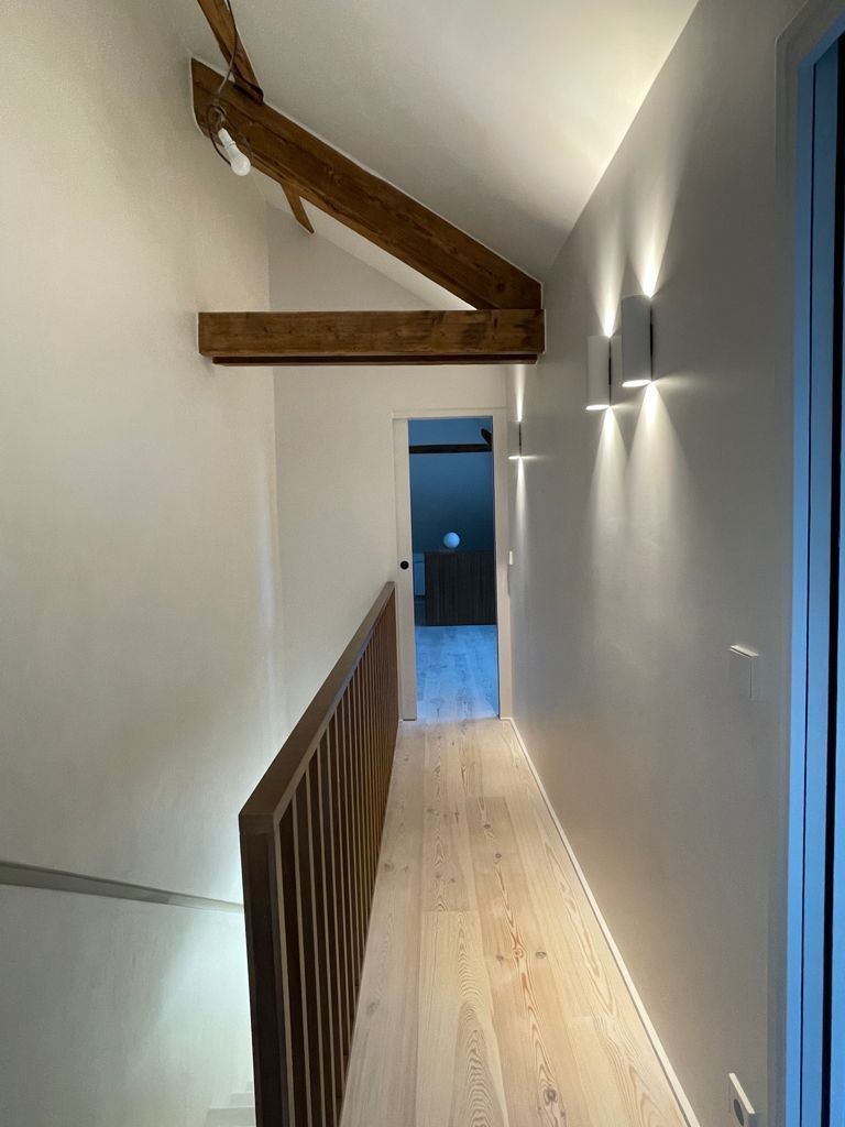 Couloir étroit avec parquet clair, poutres apparentes au plafond, rampe d'escalier en bois.