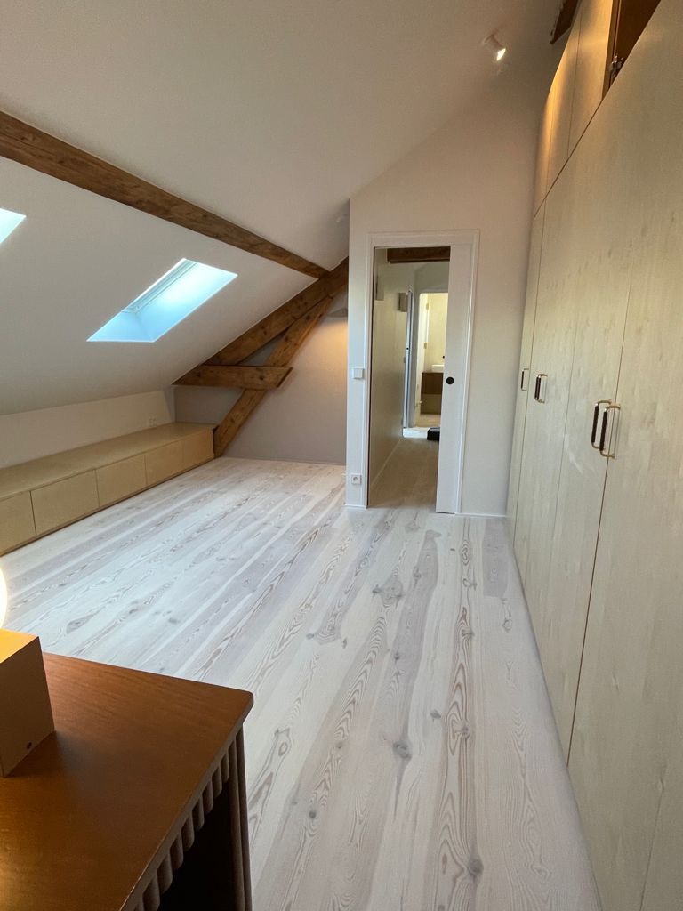 Chambre mansardée blanche avec poutres apparentes, placards intégrés et Velux.