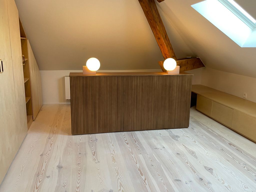 Chambre mansardée avec bureau en bois, deux lampes rondes et une fenêtre de toit.