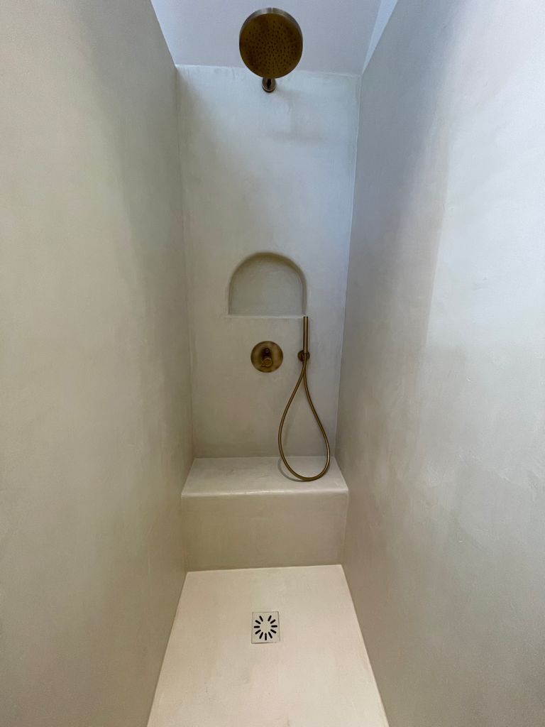 Cabine de douche blanche avec tête de douche, douchette et niche murale.