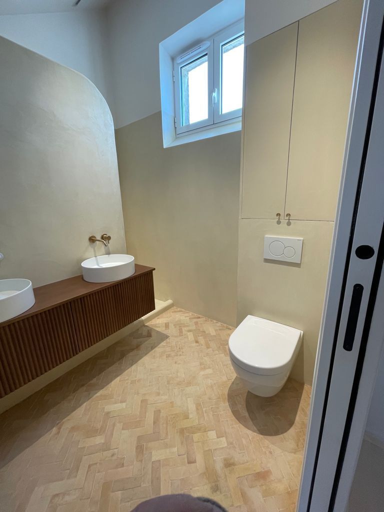 Salle de bains design avec double vasque, mobilier en bois, robinetterie dorée et parquet au sol.