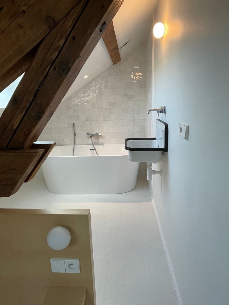 Petite salle de bains mansardée avec baignoire blanche, mur carrelé, lavabo suspendu.