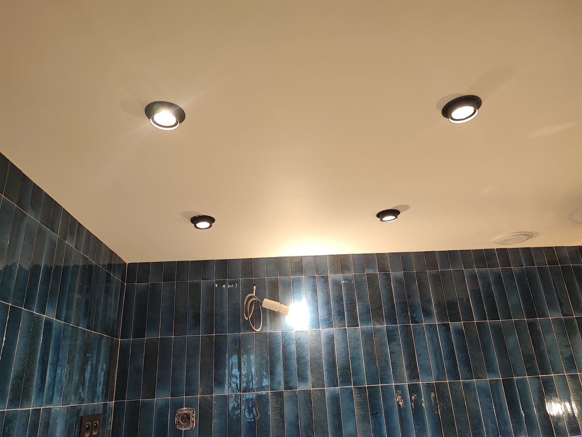 Plafond de salle de bains avec spots encastrés au-dessus de murs carrelés bleus.