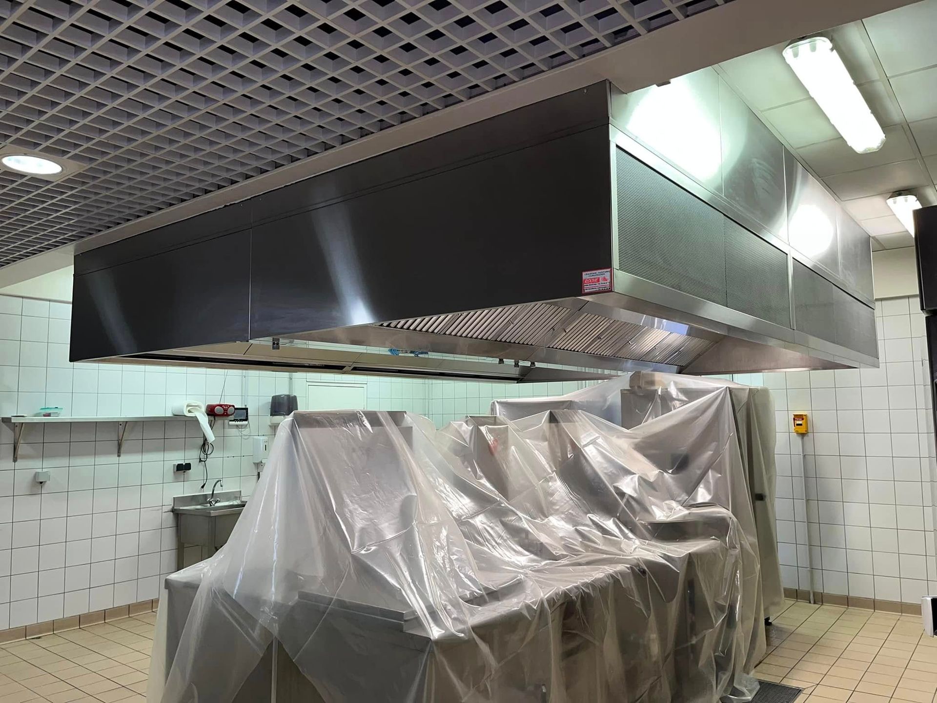 Une hotte de cuisine professionnelle est suspendue au-dessus d'équipements de cuisine recouverts d'une bâche de protection.