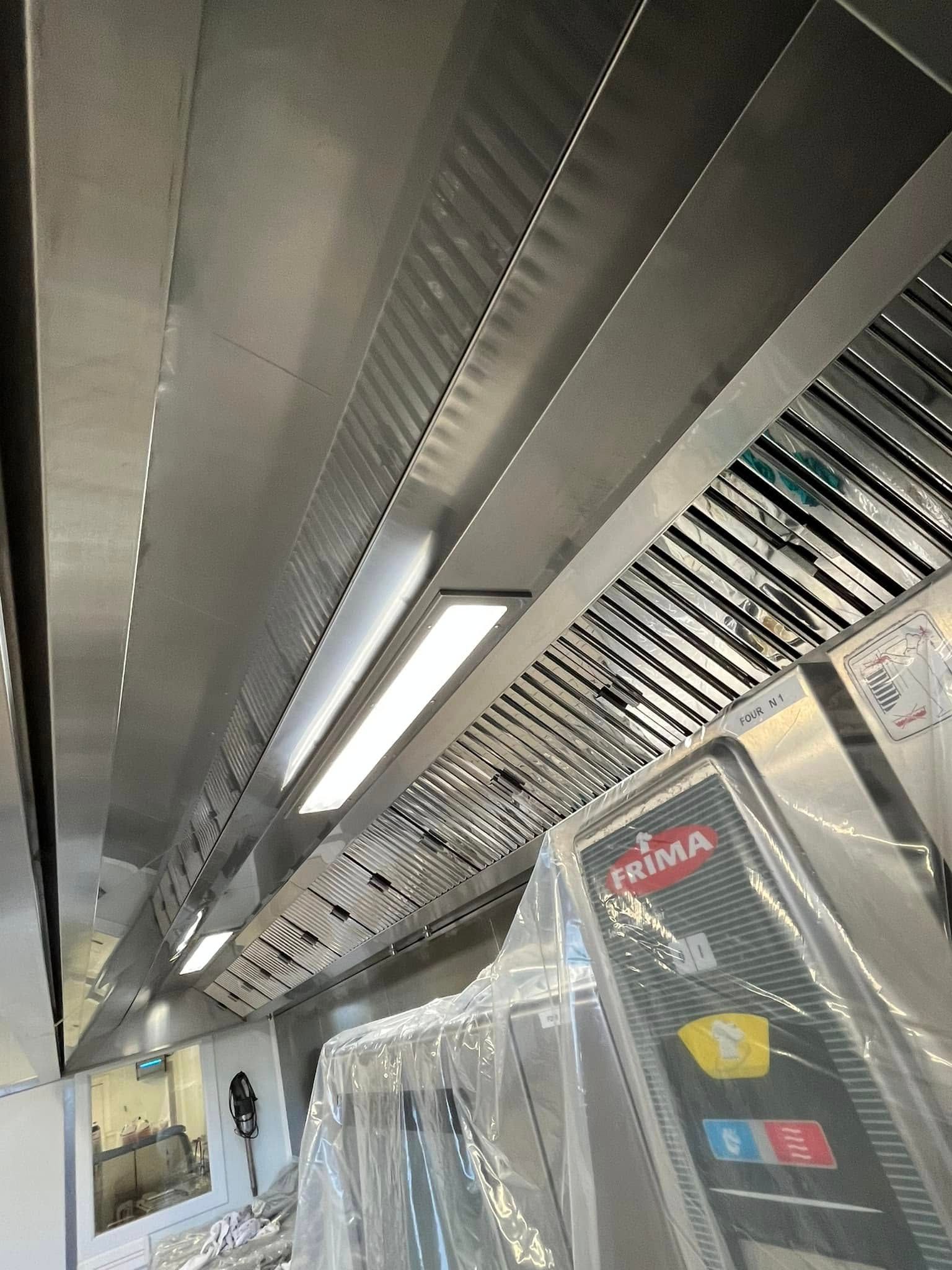 Une hotte de cuisine en acier inoxydable avec filtres industriels, placée au-dessus d'un équipement de cuisine emballé.